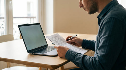 Une personne relit un document imprimé à côté d'un ordinateur portable