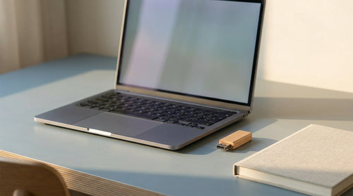 Un ordinateur portable ouvert sur un bureau clair à côté d'une clé USB